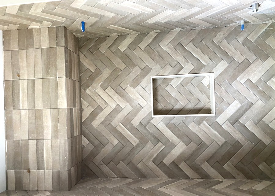 Herringbone pattern tile accent wall with built-in niche in a Hamilton bathroom renovation