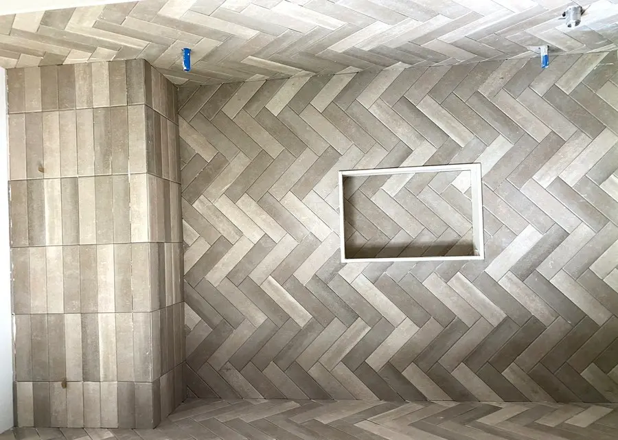 Herringbone pattern tile accent wall with built-in niche in a Hamilton bathroom renovation