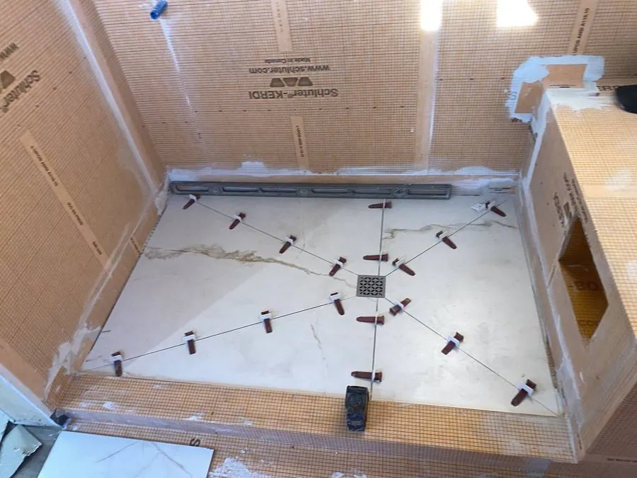 Bathroom shower floor tile installation on Schluter-Kerdi waterproof membrane, laid out from the centre drain with tile spacers and a level, Hamilton renovation