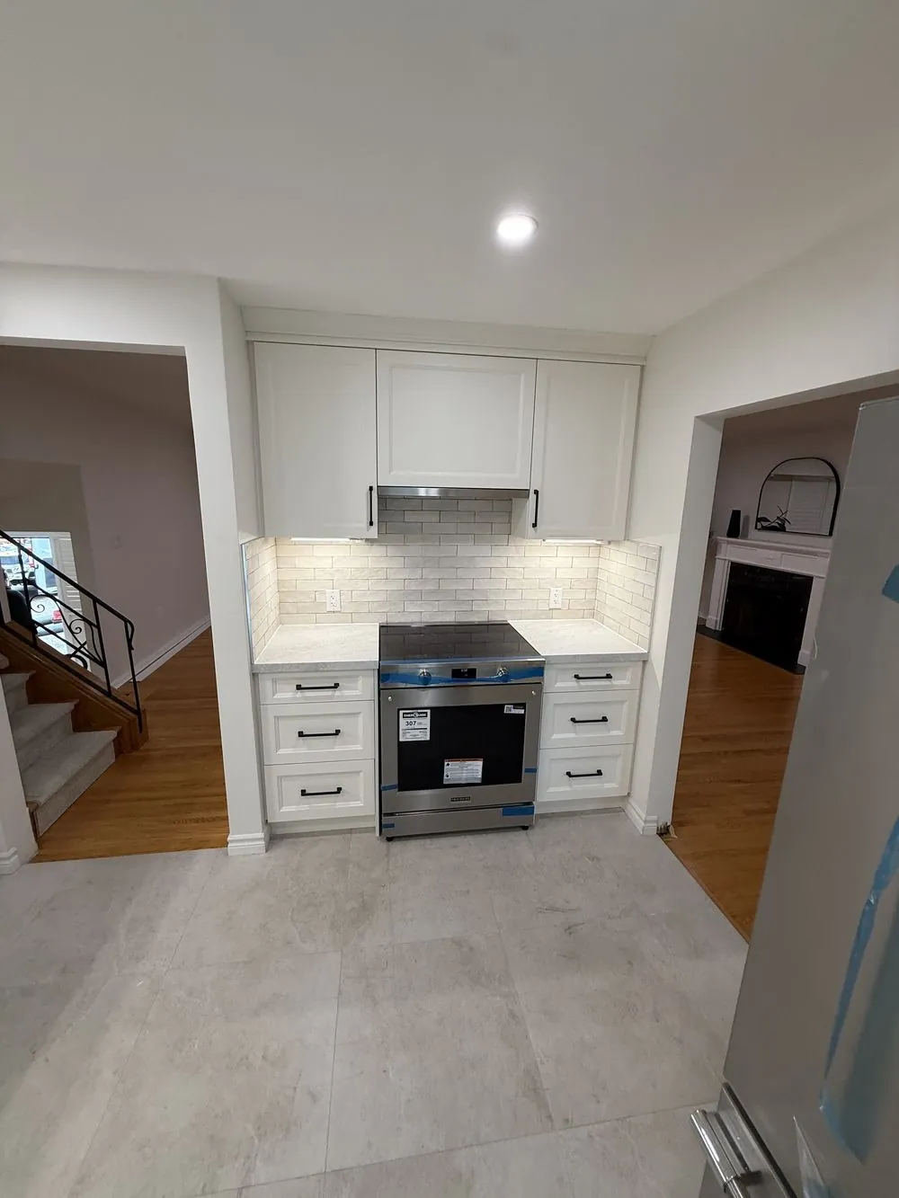 Finished Ancaster kitchen renovation with white cabinetry, subway tile backsplash and hardwood flooring visible through to the hallway